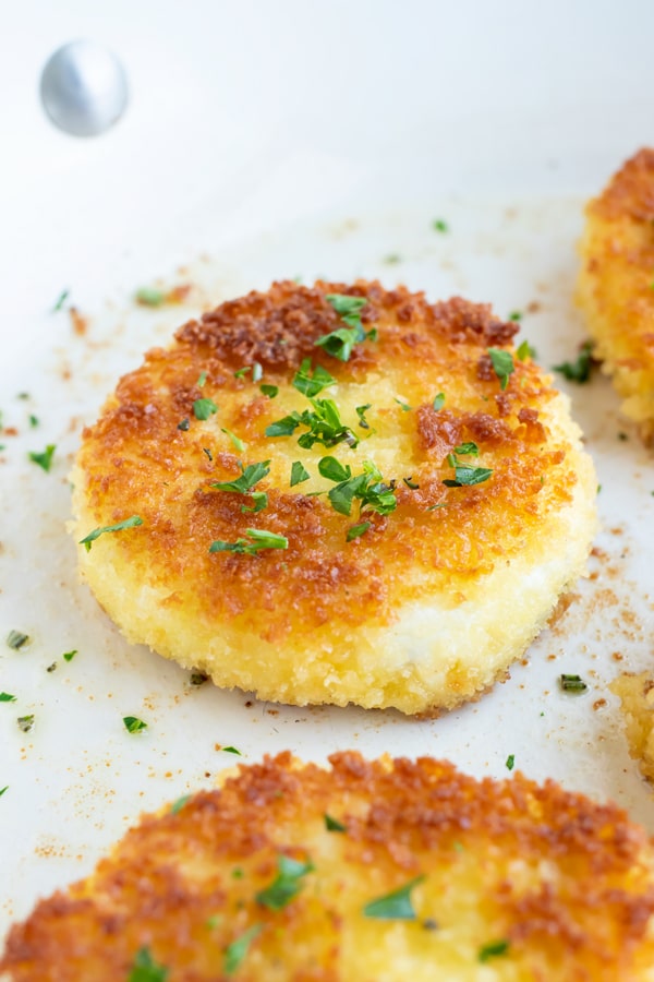 A fried goat cheese recipe with honey and herbs being seared in a skillet.
