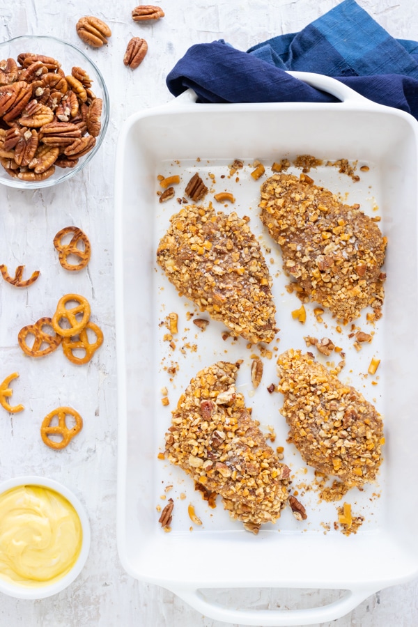 An easy baked honey chicken recipe with pretzels and pecans in a baking dish.