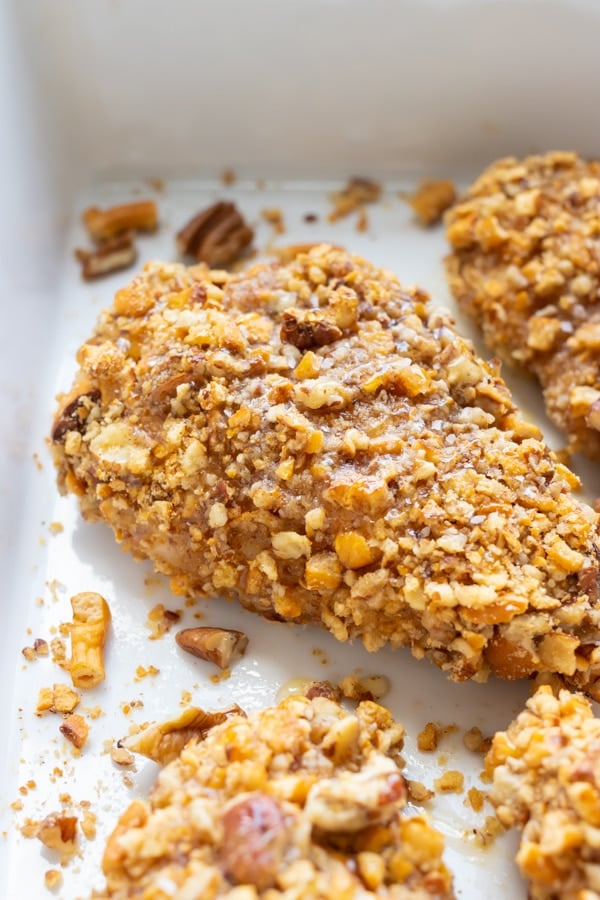 Baked honey chicken recipe with pretzels and pecans in a baking dish.