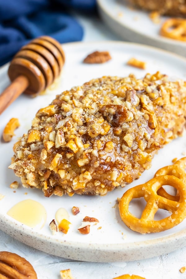 A healthy gluten-free honey baked chicken breast recipe on a white dinner plate next to pretzels and pecans.