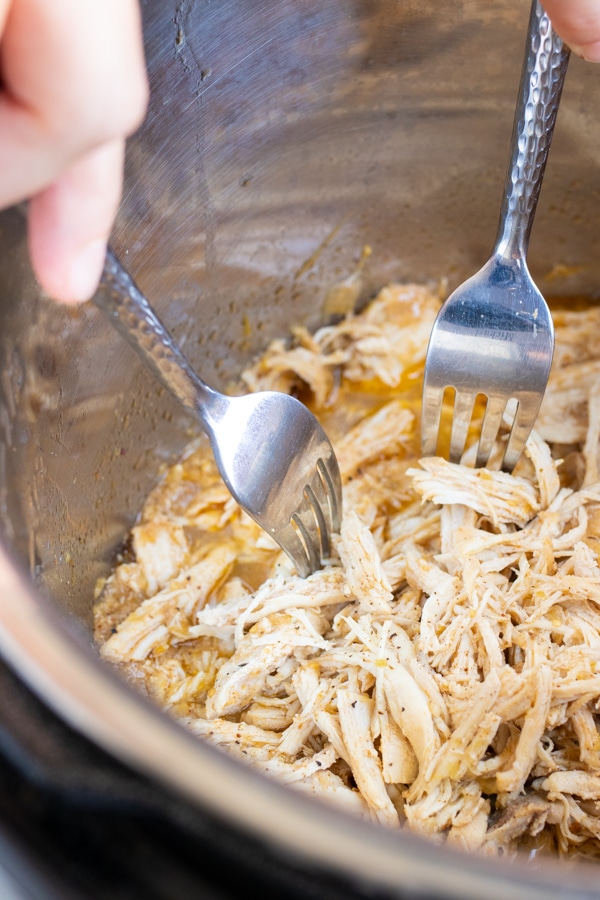 Chicken being shredded in an Instant Pot with two forks.