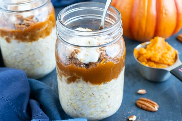 Two glass jars full of healthy pumpkin overnight oats recipe with pecans next to them.