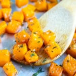 A wooden spatula picking up roasted butternut squash cubes with thyme.