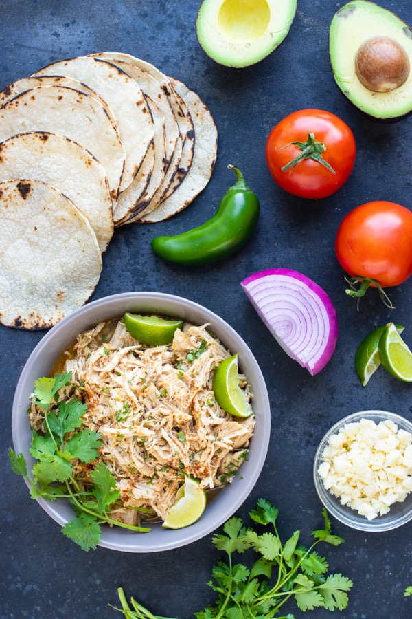 Tortillas, avocado, tomato, shredded chicken, and Cotija cheese as the ingredients for an easy chicken taco recipe.