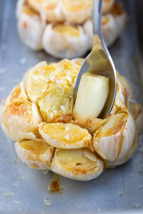 Roasted garlic in a pan with a spoon scooping out one clove.