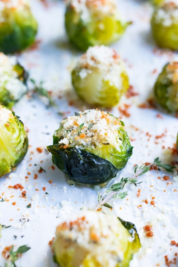 A baking sheet full of vegan roasted Brussels sprouts that are topped with grated Parmesan and fresh herbs.