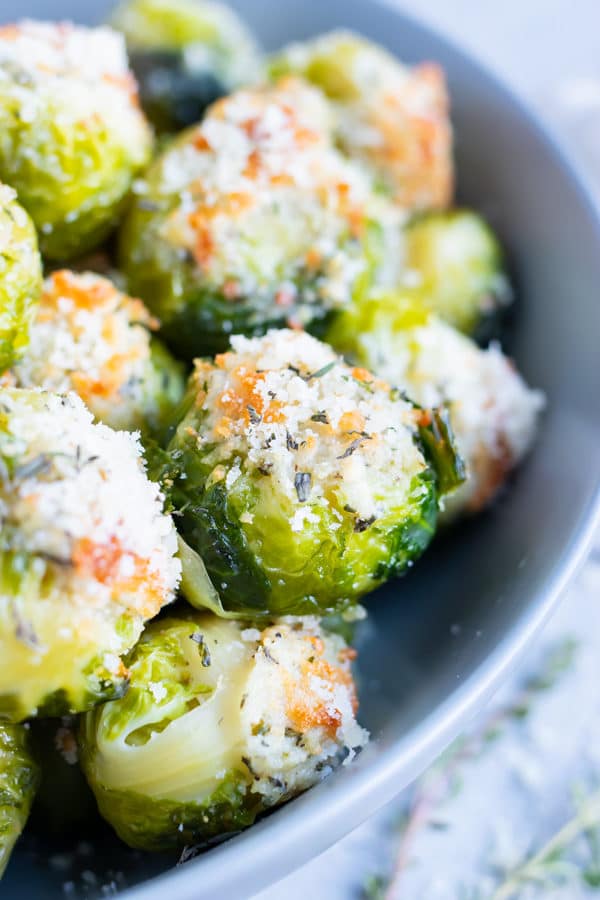The best roasted Brussels sprouts recipe with Parmesan cheese, garlic, and herbs in a grey bowl.