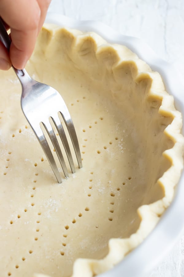 A fork piercing holes in the bottom of a gluten-free pie crust.