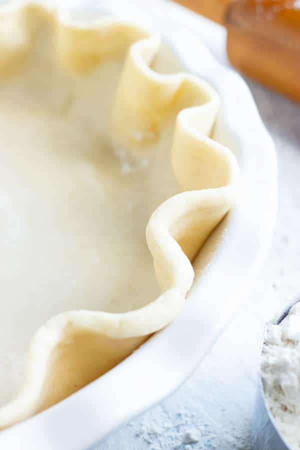 A buttery and flaky pie crust recipe in a white plate for a pumpkin pie.