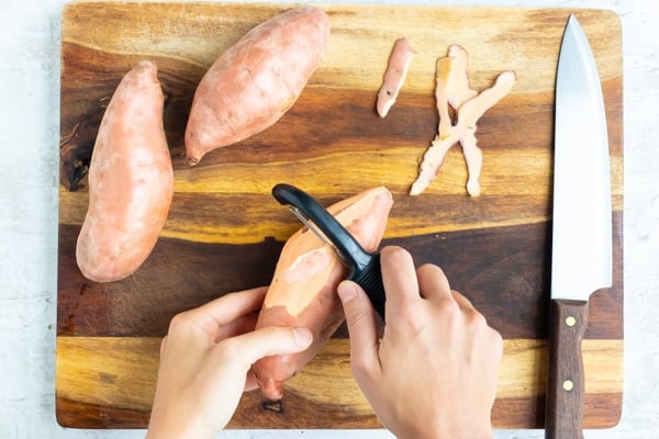 A hand showing how to peel sweet potatoes before boiling in water.