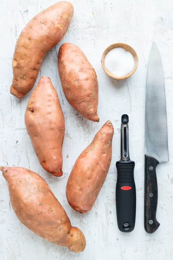 Sweet potatoes, a potato peeler, a knife, and salt as the tools and ingredients for boiling sweet potatoes.