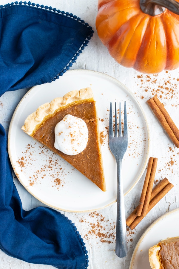 Two dessert plates with slices of the best pumpkin pie recipe next to a blue napkin and cinnamon sticks.