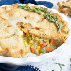 A healthy chicken pot pie recipe with a piece cut out that is full of carrots and peas.