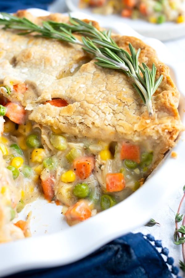 A healthy chicken pot pie recipe with a piece cut out that is full of carrots and peas.