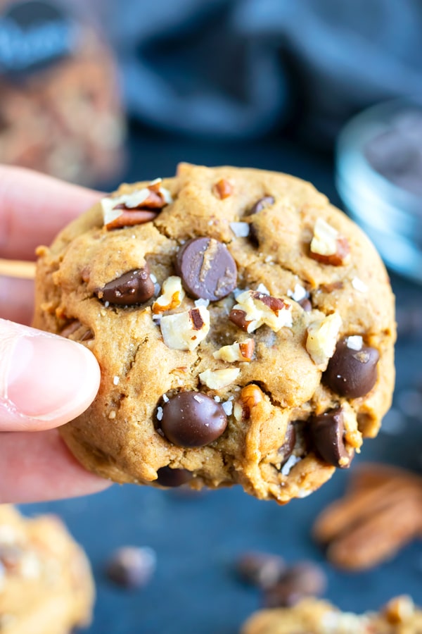 A hand holding a soft and fluffy chocolate chip cookie that is made with gluten-free flour and peanut butter.