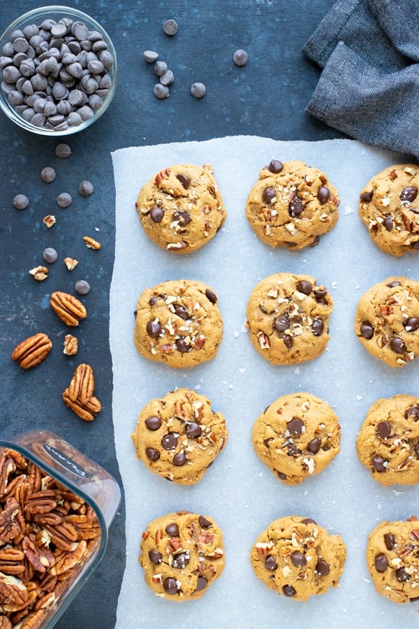 Chocolate chip cookies that have been baked in the oven next to pecans.