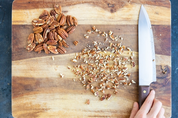 Raw pecans being coarsely chopped on a cutting board for a cookie recipe.