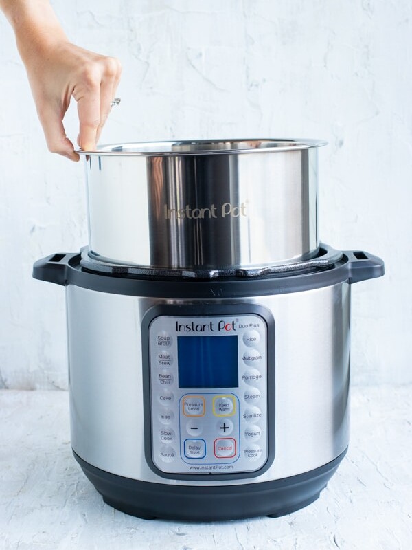 A stainless steel pot being placed into an electric pressure cooker.