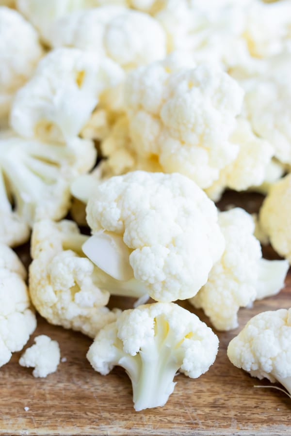 Small cauliflower florets on a wooden cutting board.