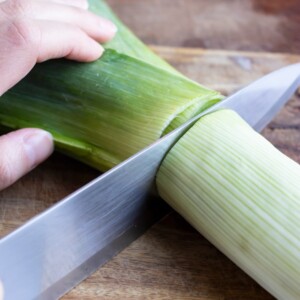 An image showing how to cut fresh leeks to use the white part for soup and discard the green part.
