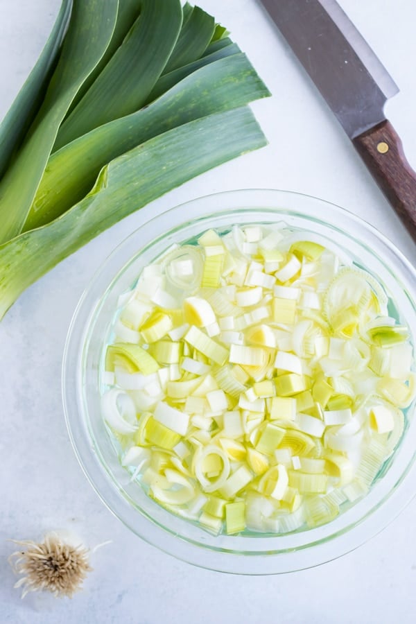 Fresh leeks that have been cut and are being cleaned in a bowl of water.