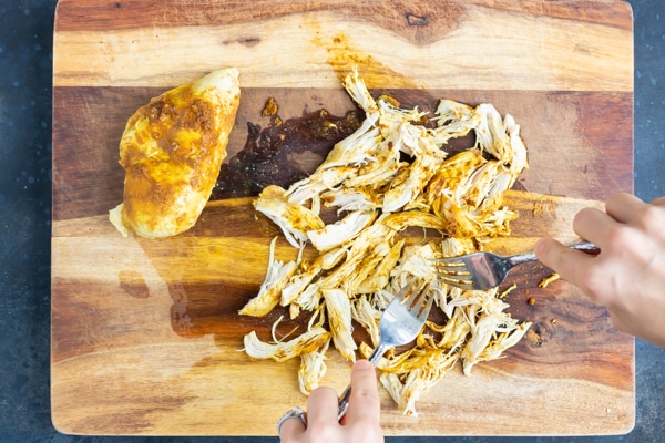 Curry chicken being shredded with two forks on a wooden cutting board.
