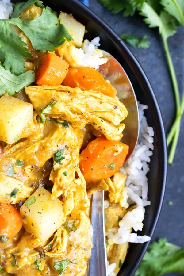 A closeup of a spoon getting a bite of yellow chicken curry with potatoes and carrots.