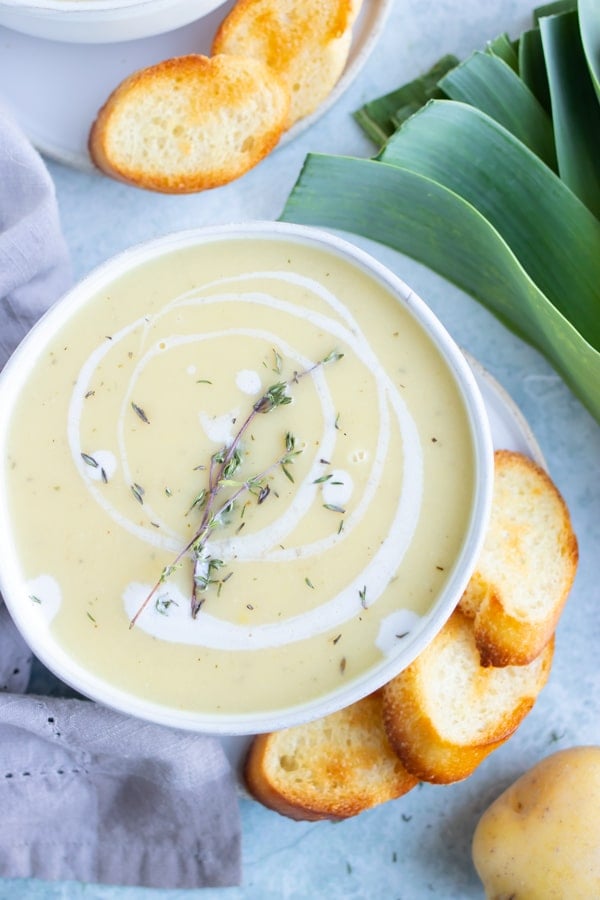 Potato Leek soup in a white bowl next to toasted baguette bread.