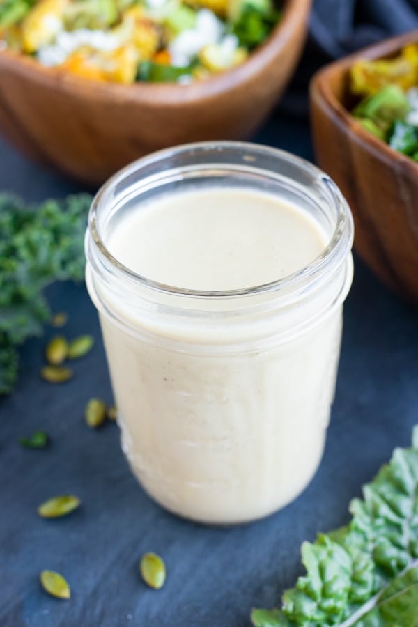 Creamy vegan tahini salad dressing in a clear glass storage jar.
