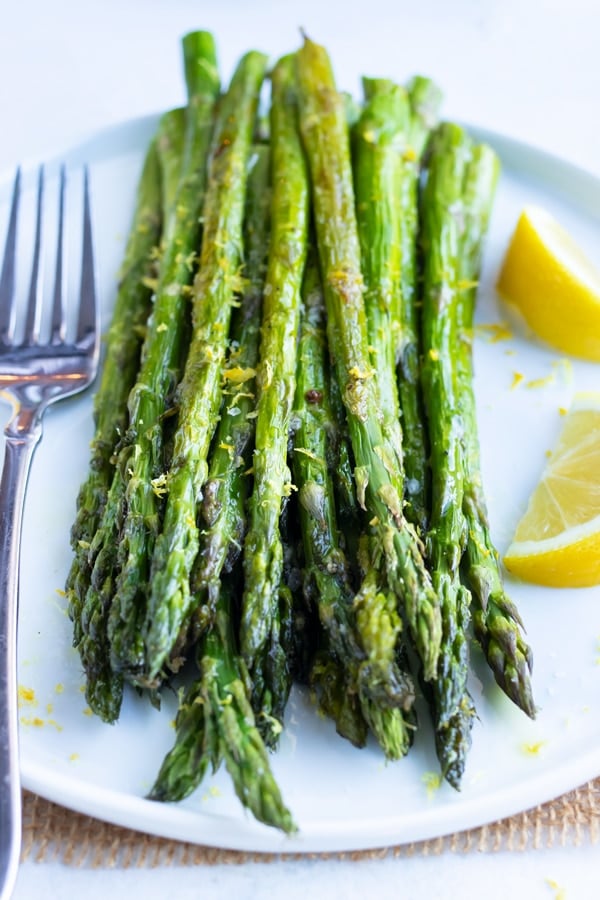 Oven-roasted asparagus with lemon and garlic sauce on a white serving plate.