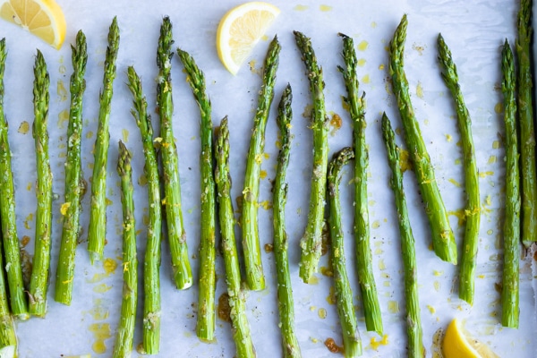 Asparagus that has been roasted in the oven on a baking sheet with lemon wedges.