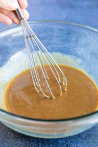 A large glass bowl with peanut butter, coconut oil, coconut sugar, and pure maple syrup being whisked together.