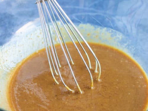 A large glass bowl with peanut butter, coconut oil, coconut sugar, and pure maple syrup being whisked together.
