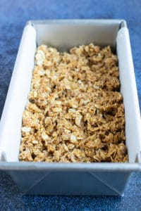 A loaf pan lined with parchment paper and full of a no-bake oatmeal bar mixture.