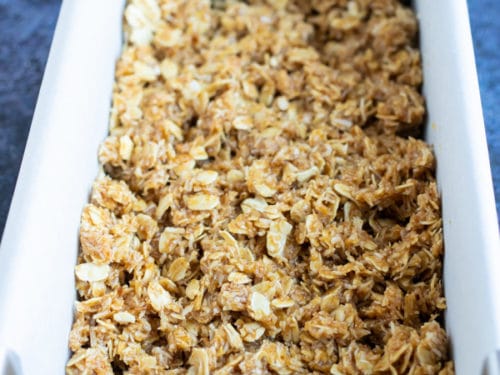 A loaf pan lined with parchment paper and full of a no-bake oatmeal bar mixture.