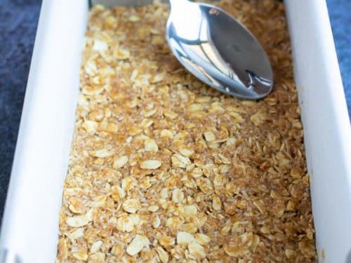 A spoon pressing down the oatmeal crumble to form the base of Samoa bars in a loaf pan.