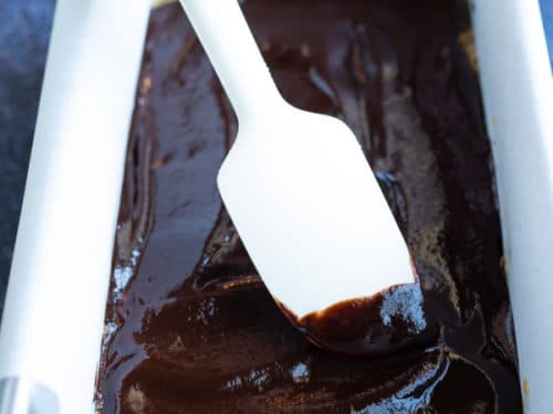 A small spatula smoothing out a chocolate glaze over no-bake oatmeal bars.
