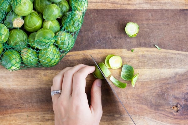 Trimming and slicing a Brussels sprout on a wooden cutting board.