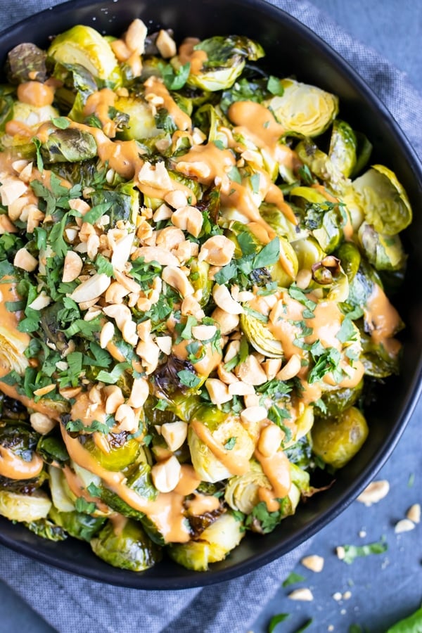 A bowl full of roasted Brussels sprouts with a peanut butter sauce and cilantro.