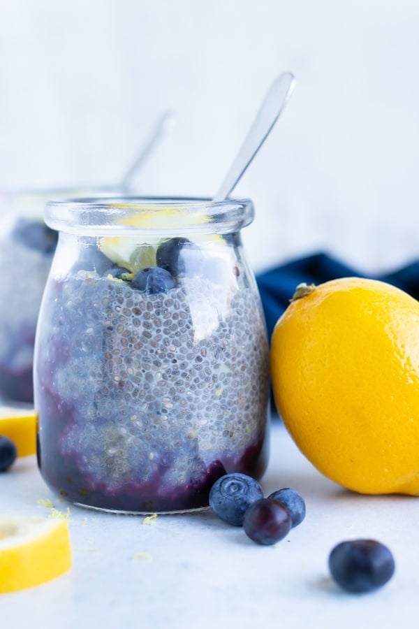 Glass jar with blue chia pudding next to a lemon and blueberries.