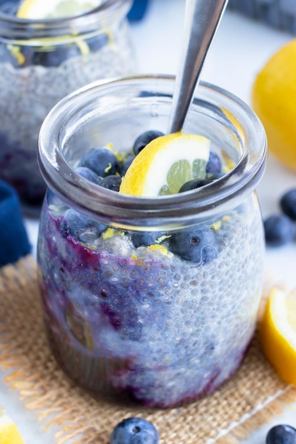 Fresh blueberries and a lemon slice on top of a glass jar full of a vegan chia pudding.