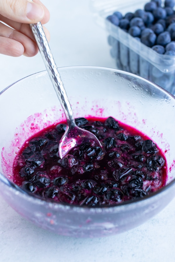 A homemade fresh blueberry jam being mixed with a spoon in a glass bowl.