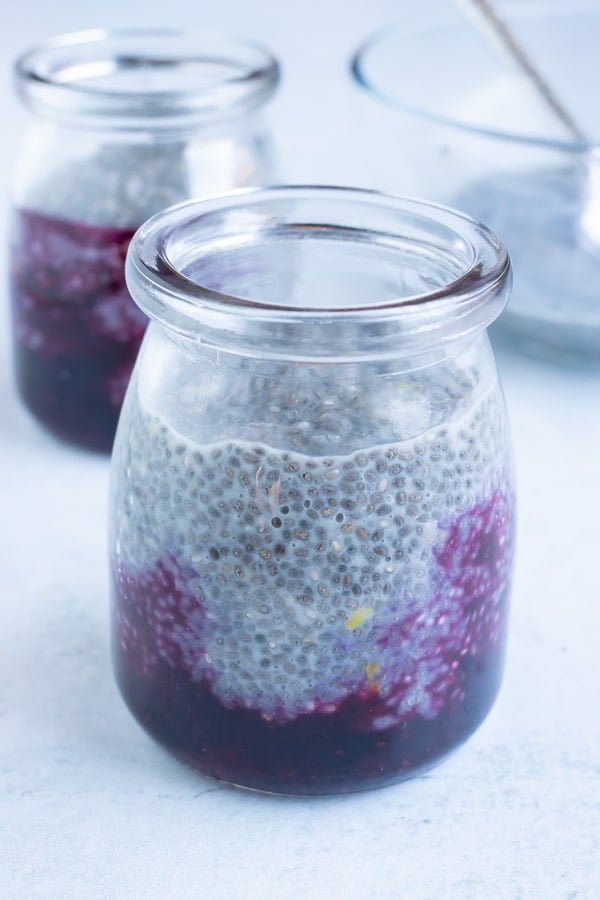 Chia pudding is added to blueberry jam in a jar.