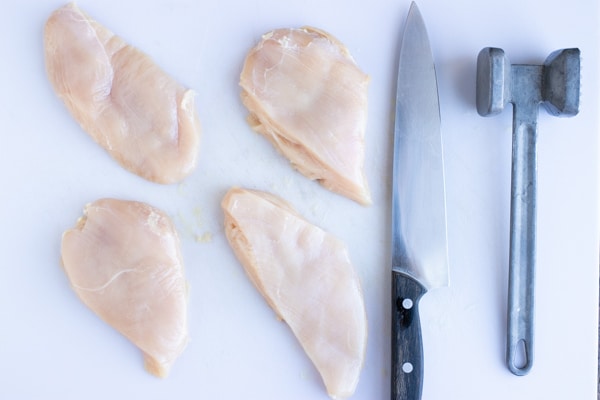Chicken breasts pounded thin and cut into 4-ounce portions next to a meat mallet.