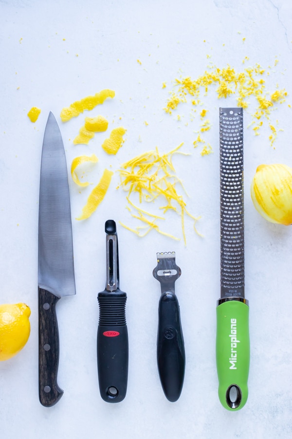 A knife, vegetable peeler, citrus zester, and microplane next to lemon peel and zest.