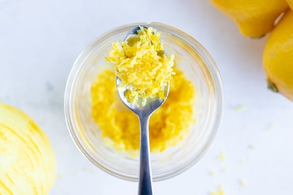 Yellow citrus zest on a spoon over a jar full of it.