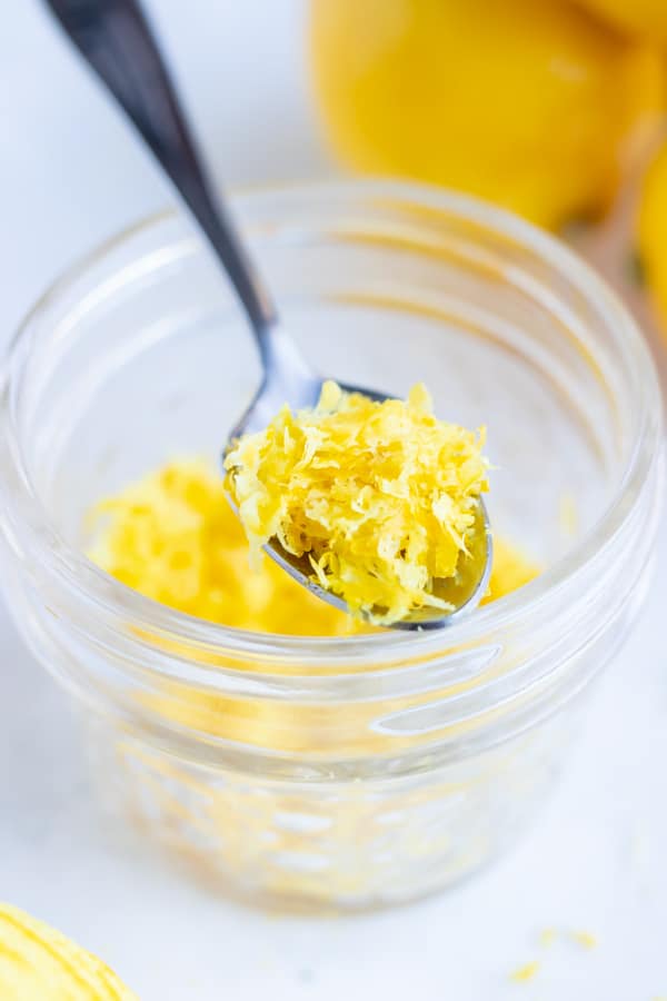 A glass jar full of lemon zest and a silver spoon scooping some out.
