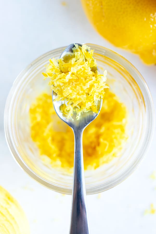 Yellow citrus zest on a spoon over a jar full of it.