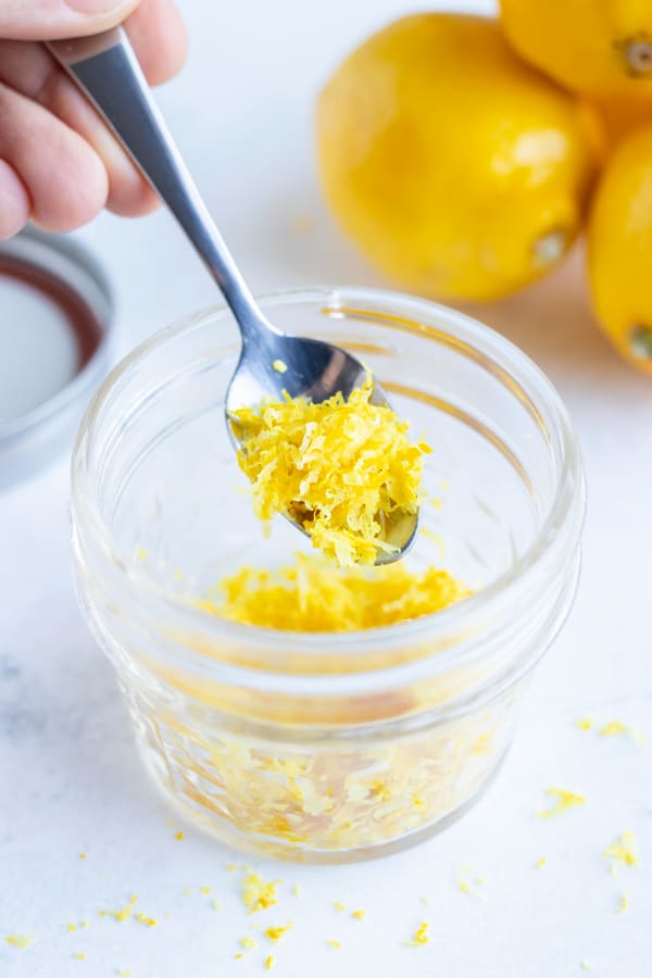 A glass jar full of lemon zest and a silver spoon scooping some out.