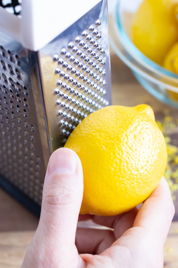 vA hand zesting a lemon using a cheese grater.